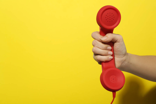 Closeup view of woman holding red corded telephone handset on yellow background, space for text. Hotline concept - Photo, Image