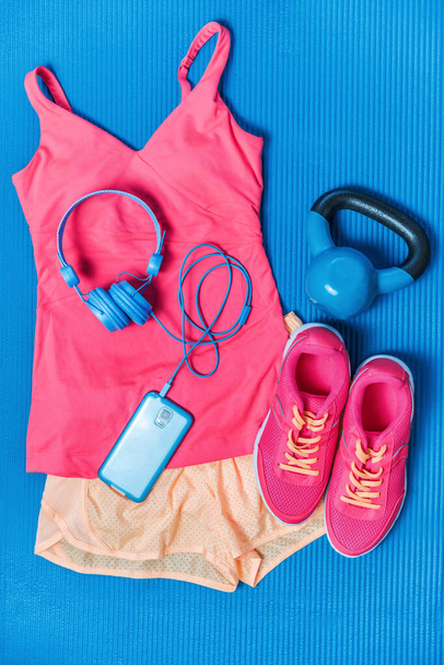Gym clothes - cute pink activewear outfit - fitness clothing, running shoes, blue headphones and mobile phone for music during training. Fashion style matching tank top, shorts, kettlebell. - Фото, зображення