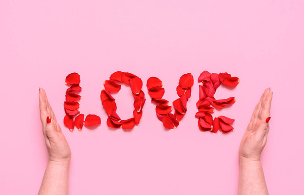 Vlak lag met liefdeswoord uit rode rozenblaadjes letters, op een roze achtergrond. Vrouwenhanden omhullen het woord liefde. Een romantisch concept voor Valentijnsdag. - Foto, afbeelding