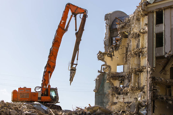 Building of the former hotel demolition for new construction, using a special excavator-destroyers against blue sky. Complete highly mechanized demolition of building structures.  - Photo, Image