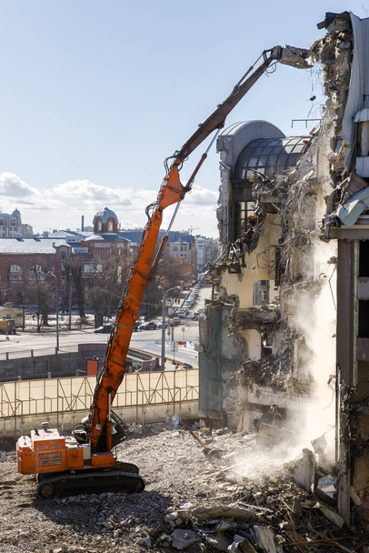 Building of the former hotel demolition for new construction, using a special hydraulic excavator-destroyer, city on background. Construction site, destruction concept - Photo, Image