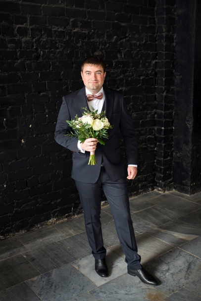 The groom in a black suit with a bouquet - Photo, Image