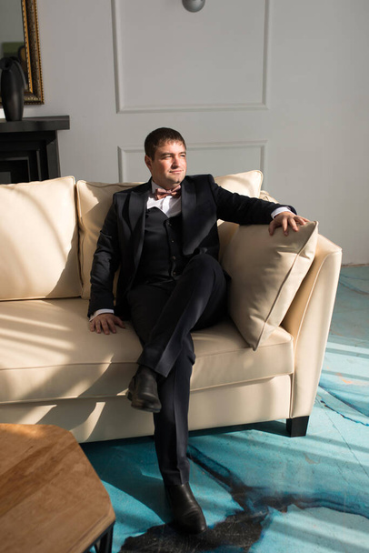 Αξιοσέβαστος άντρας με πουκάμισο και παπιγιόν κάθεται στον καναπέ. - Φωτογραφία, εικόνα