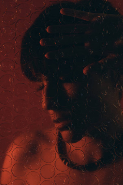 Portrait créatif d'une femme derrière un film à bulles en plastique les yeux fermés en studio - Photo, image