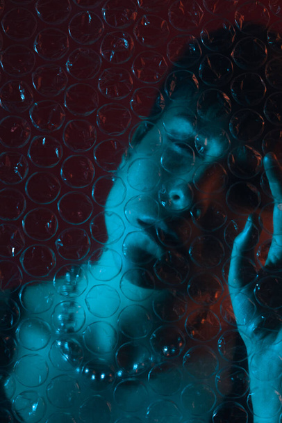 Kreatív portré egy nőről műanyag buborékfólia mögött, becsukott szemmel a stúdióban - Fotó, kép