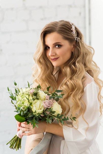 Beautiful bride in peignoir with wedding bouquet - Fotó, kép