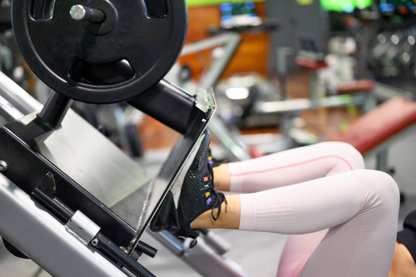 Widok bokiem dopasowanej młodej sportowca napinającej mięśnie nóg na maszynie do ćwiczeń na siłowni. - Zdjęcie, obraz