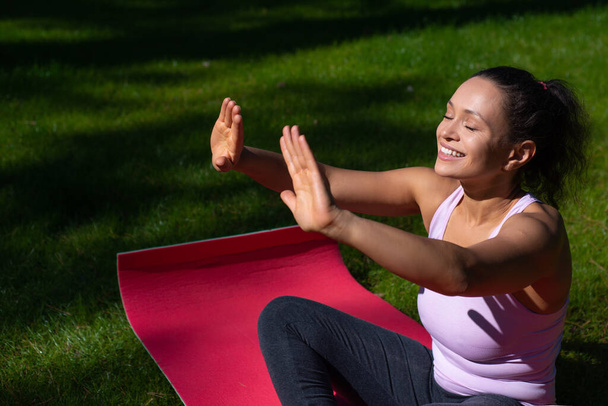 jonge gelukkig vrouw met gesloten ogen nemen zonnebaden en genieten van yoga buiten in een zonnige zomerdag - Foto, afbeelding