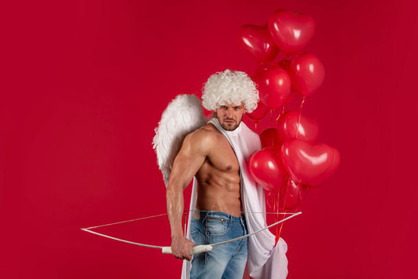 Valentines Day. Sexy male angel. Arrow of love. Handsome athlete man with angels wings. Cupid, amour, cupid. February 14. Isolated on red. - Фото, изображение