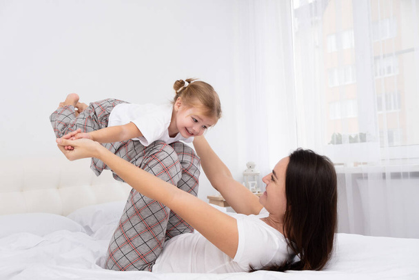 adult mother play with little active daughter in bed at home, having fun, activity with children - Photo, Image