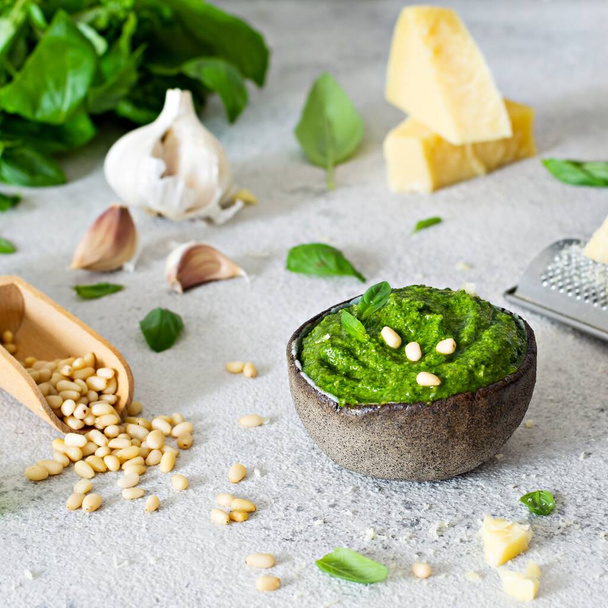 Green pesto in a bowl made from fresh basil leaves, pine nuts, parmesan, garlic and olive olia on a light background. Popular Italian dressing for salads, pasta and pizza. - Foto, afbeelding