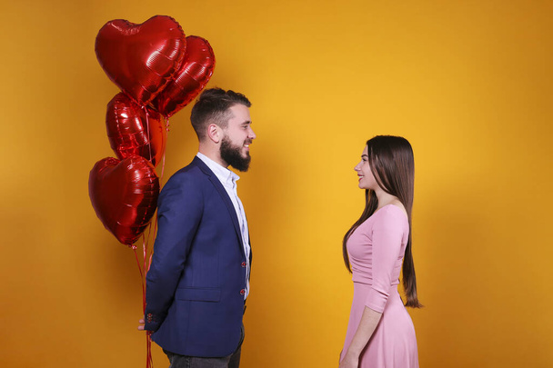 Happy Valentine's day concept. Studio shot of couple in love holding a heart shaped balloon. Portrait of bearded guy and girl in pink dress posing over yellow wall background. Copy space, casual style - Photo, image