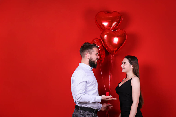 Bearded man proposing to his beautiful girlfriend on st Valentine's day. Guy with perfectly groomed facial hair and young woman in tight black dress getting engaged. Yellow wall background, copy space - Photo, image