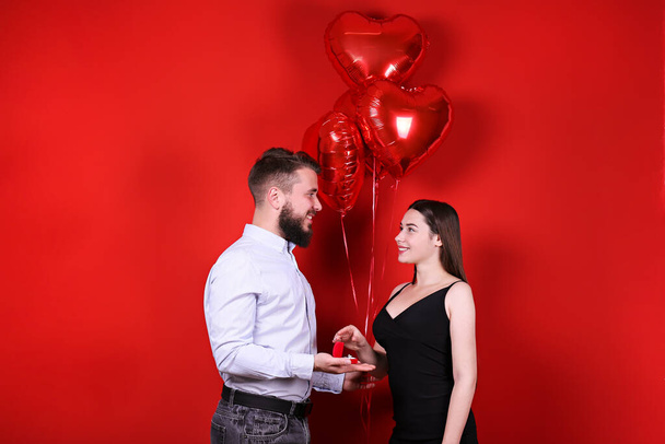 Bearded man proposing to his beautiful girlfriend on st Valentine's day. Guy with perfectly groomed facial hair and young woman in tight black dress getting engaged. Yellow wall background, copy space - Photo, image