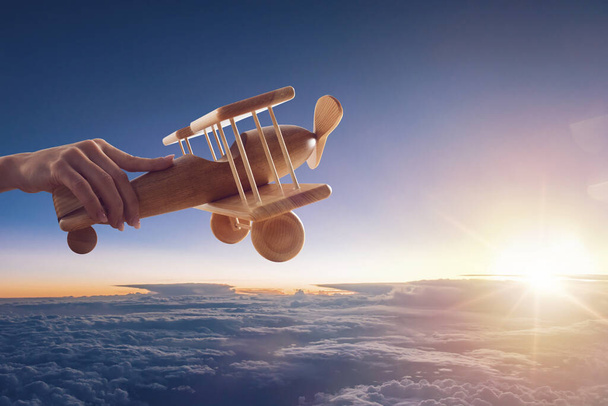 Blisko zabytkowego drewnianego samolotu zabawkowego, trzymanego jedną ręką, lecącego nad chmurami na niebie - Zdjęcie, obraz