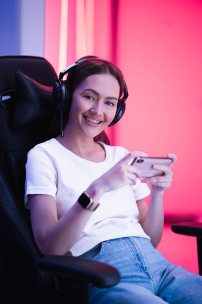 Cybersport jugador jugando juego móvil en el teléfono inteligente sentado en una silla de juego en la sala de color de neón. - Foto, Imagen