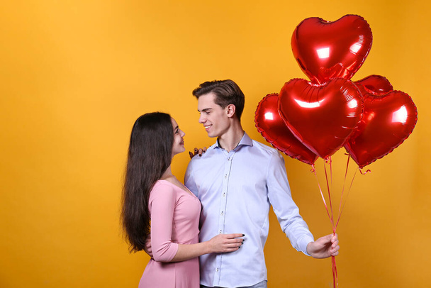 Happy Valentine's day concept. Studio shot of couple in love holding a heart shaped balloon, showing affection. 14th february - the lovers day. Yellow wall background, copy space, front view portrait. - Photo, Image