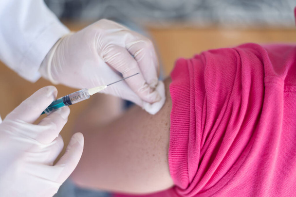Νεαρή γυναίκα ιατρός με προστατευτική μάσκα, που ενίεται ή προετοιμάζεται για την ένεση εμβολίου κατά του κορωναϊού ή του ncov 19 ή του covid στο βραχίονα του ασθενούς - Φωτογραφία, εικόνα