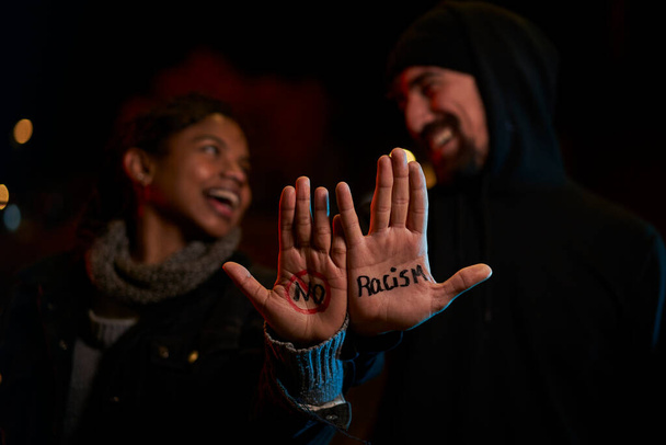 Ein junger weißer Mann und eine junge schwarze Frau lächeln und zeigen eine handgeschriebene Botschaft gegen Rassismus. - Foto, Bild