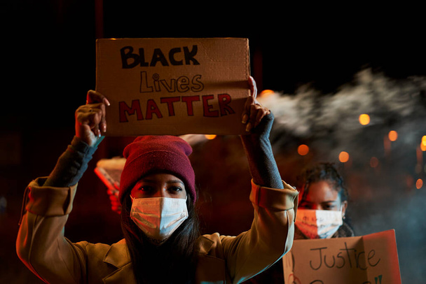 Αφροαμερικανίδες διαδηλώνουν κατά του ρατσισμού. Διαδηλωτές σε μια πόλη με πανό που μάχονται για τα δικαιώματά τους. Κοιτάζουν μια σοβαρή κάμερα που κρατάει πανό. Μαύρη ύλη ζωής. - Φωτογραφία, εικόνα
