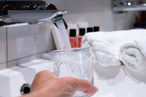 kraan met stromend water, hand en drinkglas - Foto, afbeelding