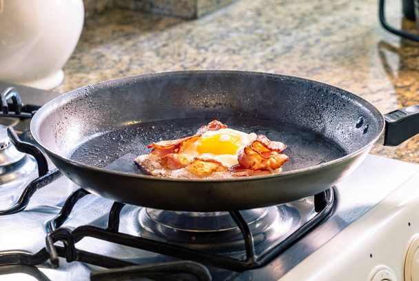 Uovo fritto con pancetta nella padella nera. Focus selettivo. - Foto, immagini
