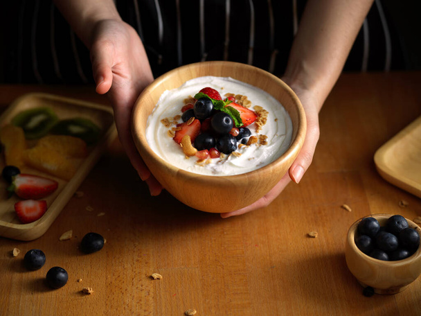 Вид сверху женских рук, держащих миску с зернолой с натуральным греческим йогуртом и свежими ягодами  - Фото, изображение
