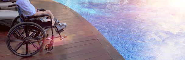 Woman sits on Wheelchair and wear Orthopedic Boot from broken leg. Disable patient travel to pool resort for rehabilitation recovery. Concept Wish to walk, swim, fly again - Photo, Image