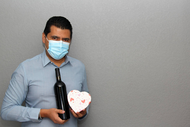 Valentine 'ın yeni normalliği. Mavi gömlekli Latin adam, klinik koruma maskesi, kırmızı şarap ve gözlük. - Fotoğraf, Görsel