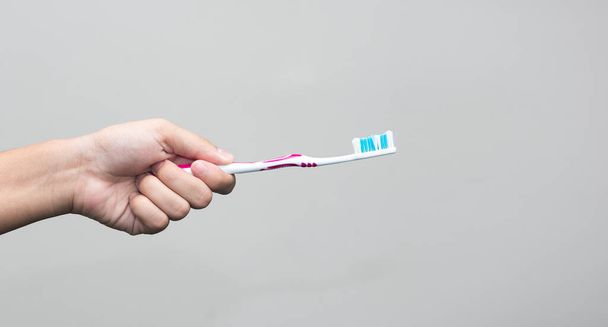 Ένας άντρας με μια οδοντόβουρτσα στο χέρι απομονωμένος σε γκρι φόντο. - Φωτογραφία, εικόνα