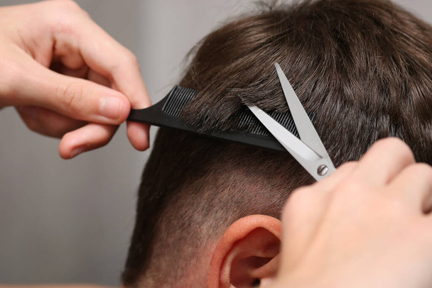 detailní záběr na ruce držet nůžky a hřeben při stříhání vlasů muže. Holičství. Hnědé vlasy jsou krátké. - Fotografie, Obrázek