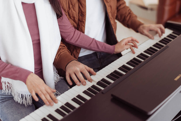 Cropped image of loving couple playing piano together. Young couple love in sweater enjoying and playing music together. - Photo, Image