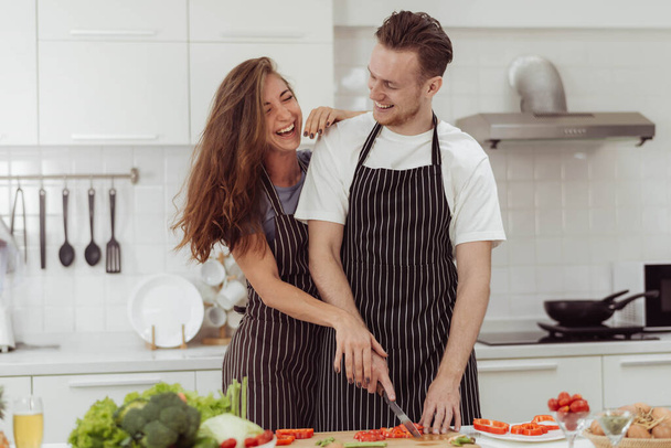 Счастливая пара любит готовить вместе на кухне. Молодой любящий мужчина и женщина смеются во время приготовления здоровой пищи дома. - Фото, изображение