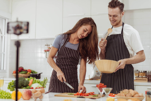 Blogger und Youtuber-Konzept: Glückliche Paare lieben es, Videos aufzunehmen, während sie gemeinsam in der Küche kochen. Liebevoller Lebensstil für Mann und Frau zu Hause. - Foto, Bild
