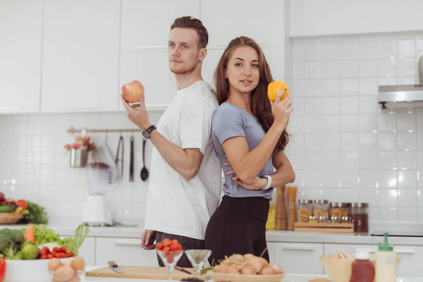 Glückliches Paar liebt es, gemeinsam in der Küche zu kochen. Junge liebevolle Mann und Frau stehen und halten Früchte in der weißen Küche Zimmer. - Foto, Bild