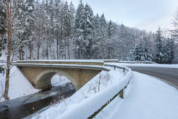 Wild river in winter with old stone bridge at Zemska Brana nature reserve, Orlicke hory, Eagle mountains, Eastern Bohemia Czech republic. Beautiful frosty day. Snowy weather in mountain. Popular place - Zdjęcie, obraz