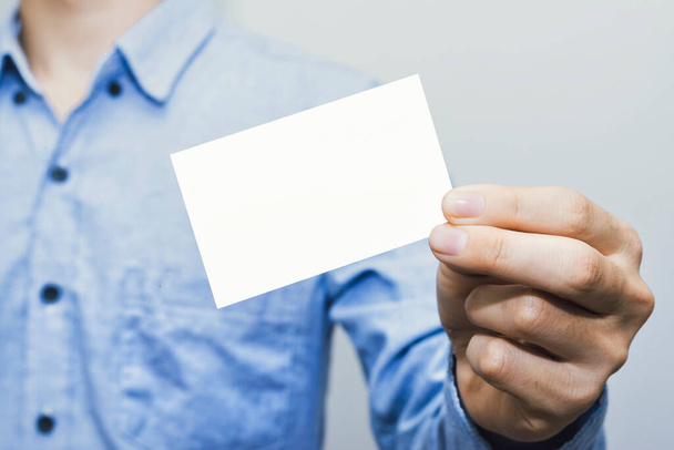 Hombre sosteniendo la tarjeta de visita blanca sobre fondo de pared de hormigón, plantilla de maqueta - Foto, Imagen