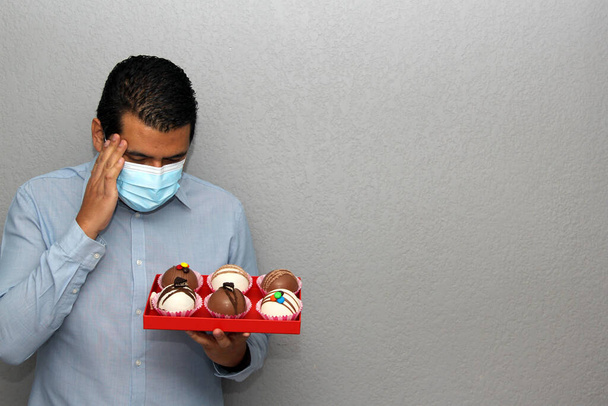 San Valentín en un hombre covid-19 pandemic.latin con máscara de protección y bombas de chocolate y regalos - Foto, imagen
