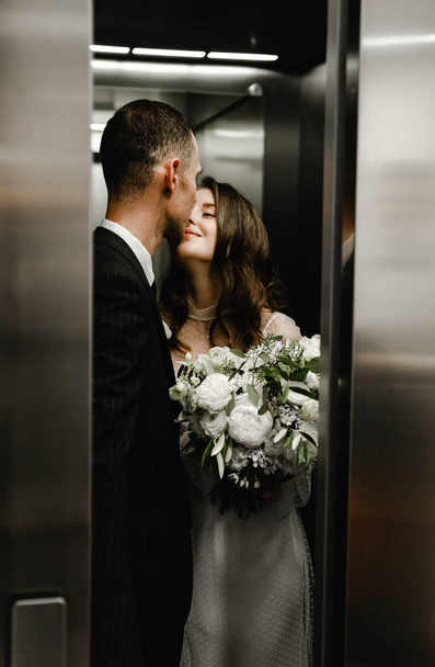the newlyweds kiss as the elevator doors close. the groom and the bride are happy. wedding couple ride the elevator to the wedding ciremonium - Photo, Image