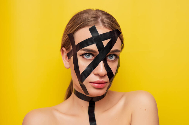 Portrait of a girl in bdsm style in duct tape, fashion, cosmetology, on a yellow background - Valokuva, kuva