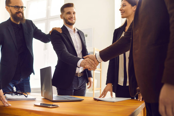 Smiling young business partners shaking hands after successful negotiations in office - Фото, изображение