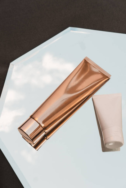 Dois de branco e ouro tubos cosméticos no fundo do espelho, produto de beleza, marca pacote mockup, minimalista, vista superior - Foto, Imagem