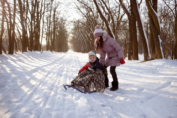 Una bambina felice di etnia caucasica tiene una slitta in cui è seduto suo fratello minore. Divertimento invernale per la famiglia. - Foto, immagini