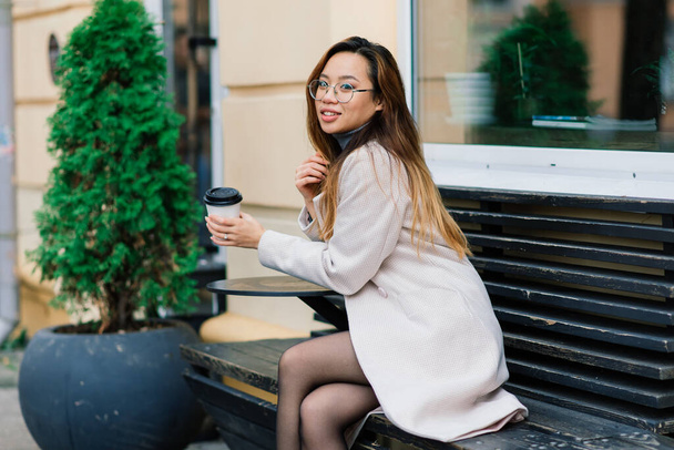 Belle jeune étudiante chinoise tenant une tasse de café dans la rue - Photo, image