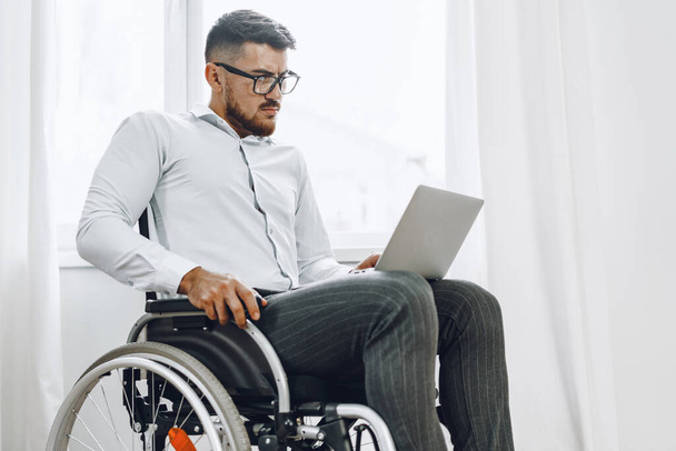 Businessman sitting in wheelchair and using laptop - Fotoğraf, Görsel