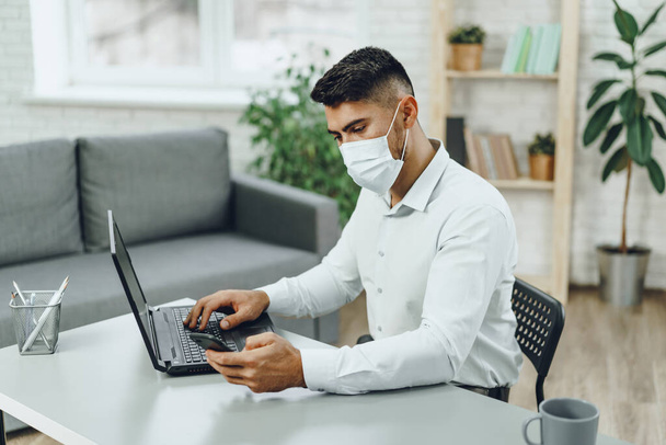 Young businessman sitting at his working desk with medical mask on - Foto, immagini