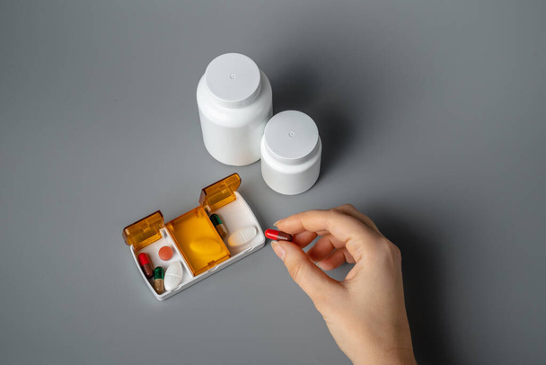Woman holding a pill in her hand. The young woman took the pill from the pill box. Healthy lifestyle. Pills on a gray background. Tablets for breakfast, lunch and dinner. - Photo, Image