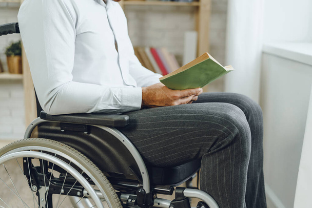Disabled man in wheelchair reading a book indoors - Fotoğraf, Görsel
