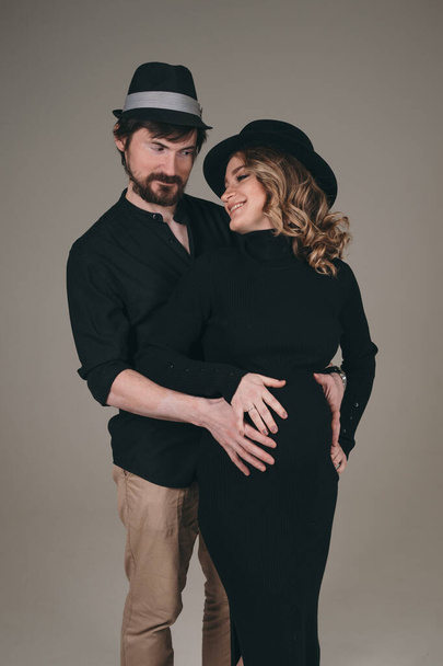 A happy man stands next to his pregnant girlfriend. loving parents are waiting for the birth of a baby. Husband hugs his pregnant wifes stomach - Фото, изображение