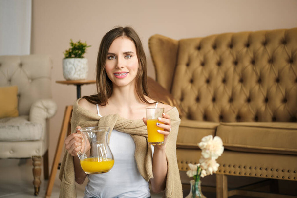 Smiling girl with braces holds glass and jug with juice in hands - Foto, Imagen